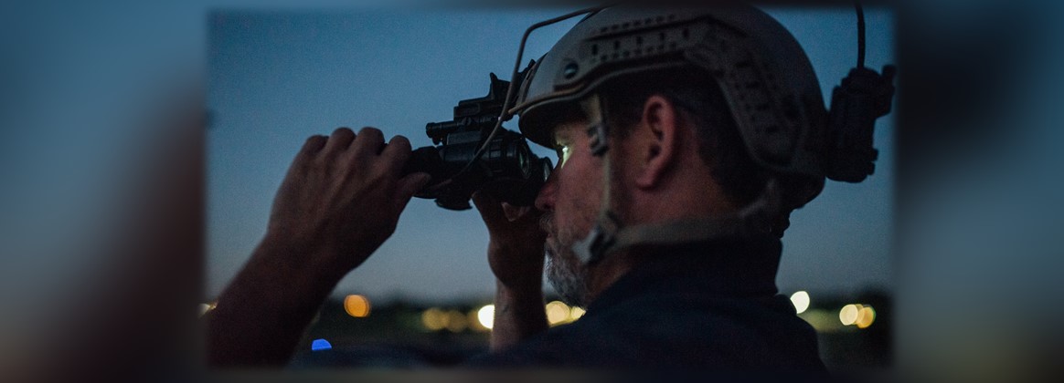 A man looks through night vision goggles.